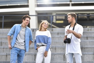 Three happy friends talking taking a conversation on the street in a sunny day with buildings in