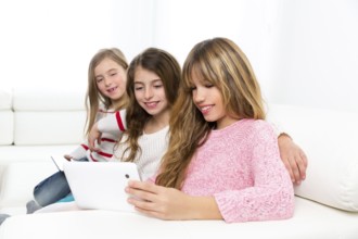 Three kid sister friends girls group playing together with tablet pc on white sofa