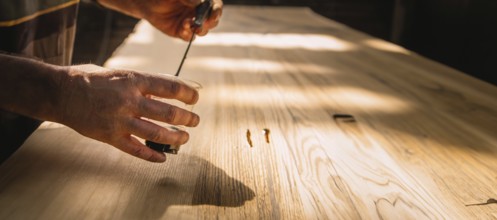 Close-up of hands working on a wooden tabletop, with sunlight creating a serene working environment