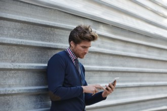 Young businessman texting smartphone phone on the street metal fence