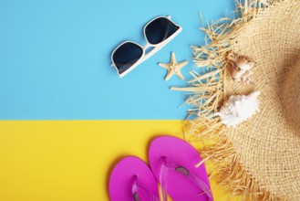 Straw hat sunglesses flip flops and shells on yellow and blue background vacation travel planning