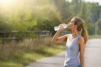 Young woman drink water while jogging outdoors