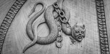 Devil snake symbol. Fantasy magic creature on an old door, 12th Century Abbey, Italy, Europe