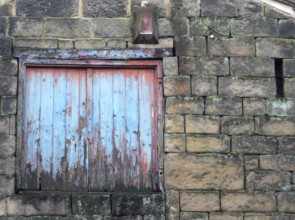 Boarded window with decaying blue painted shutters with rotting wood in a derelict abandoned house