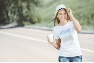 Beautiful young woman walking with a disposable coffee cup, drinking coffee and smiling against the