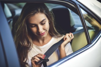 Beautiful woman with phone smiling while sitting on the back seat in the car