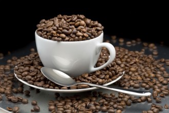 Cup and saucer full of coffee beans with a spoon on a black background