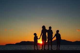 Silhouette of a family with children against the backdrop of the setting sun and sea in Montenegro