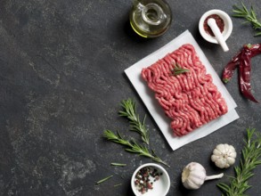 Fresh raw minced beef on backing paper and cutting board and ingredients over black cement