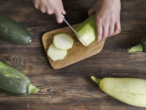 Zucchini harvest. Woman slices zucchini on wooden table. Farm organic zucchini harvesting