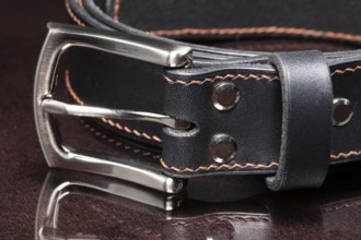 Black leather belt with a metal buckle on a dark background close-up