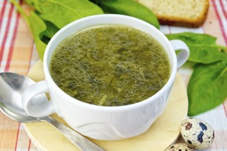 Soup of green nettles, sorrel, spinach, rhubarb leaves on a round wooden board, bread, quail eggs,
