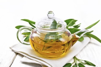 Herbal tea with sage in a glass teapot on a napkin on wooden board background