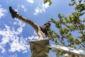 Low angle view of a caucasian man on the top of a ladder standing on one leg. as he enjoying