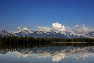 The Canadian Rockies and bright blue sky are reflected in a lake near Canmore, Alberta, Canada,