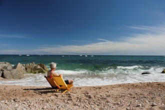 Elderly man at orange and yellow chairs on the tranquil beach