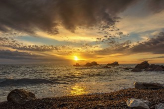 Dramatic sunset sky over beach rocks and waves, Adriatic Sea