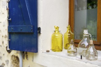 Still life with old glass bottles in window with blue shutters in France