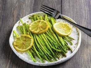 Close up view of grilled asparagus and slice of lemon in craft trendy plate on brown wooden table
