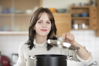 Woman in the kitchen lifts the lid off a pot with a lid, energy saving, environmentally friendly