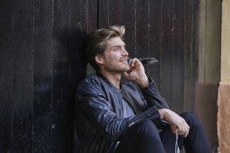 Young man with smartphone earphones sitting in the street black door