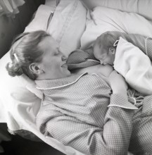 1950s mother nursing her baby. A young woman breastfeeding her baby while lying in bed at home.