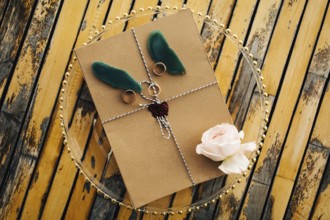 Beautiful brown envelope tied with a rope with rings, a rose and petals lies on a transparent tray