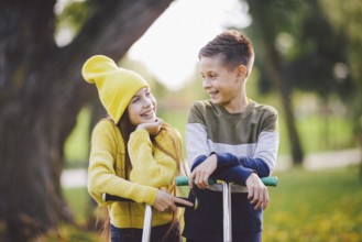 Twins 10 years old in bright clothes spend time actively together in autumn park riding kick