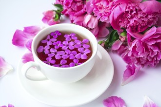 Creative layout with pink peonies flowers and cup of tea on bright table. Spring Seasonal