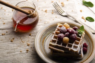 Belgian waffles served with raspberries and mint leaf dusted with powdered sugar on white wooden