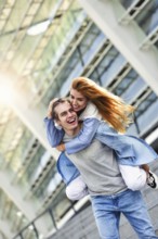 Man giving his pretty girlfriend a piggy back at street smiling at each other on a sunny day