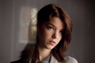 Sad thoughtful young woman behind a window