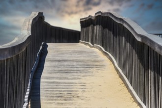 Wooden walkway bridge covered with sand, leading to infinity point