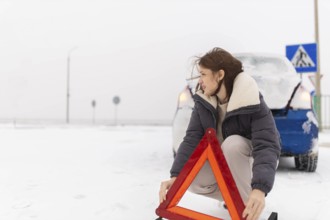 A woman sets up a warning triangle on a snowy road next to a parked car