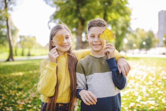 Happy Caucasian siblings enjoying in autumn day in park, sunny weather. Kids having fun holding