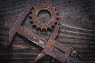 Rusted age-old measuring calipers with gear wheel on vintage dark wooden background construction