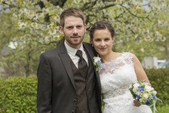 Bride and groom stand in the park in front of a blossoming fruit tree, Austria, Europe