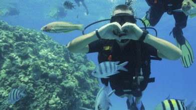 Scuba diver makes heart with his hands underwater during scuba diving at coral reef