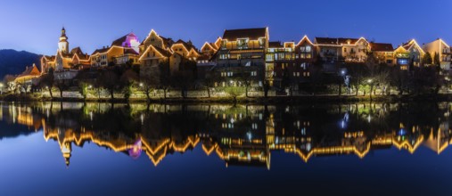 Christmas illuminated house facade of Frohnleiten reflected in the river Mur, panoramic shot, blue
