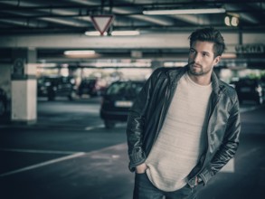 Handsome muscular man in casual clothing on background of parking