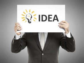 A business man holding a paper in front of his face with the text idea