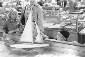 Toys in the 1950s. At a department store a boy is curious of the nice sailboat model floating in