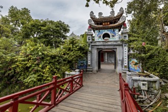A richly decorated temple with a wooden walkway, surrounded by lush greenery and Asian