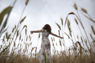 Happy woman in a floral dress stands amidst golden wheat, enjoying the serene landscape