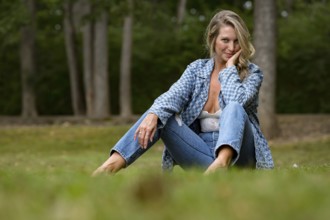 A beautiful blonde model enjoys the late summer sun outdoors. Surrounded by lush greenery and soft