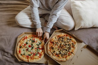 Bird's-eye view of pizzas on bed, person casually sitting