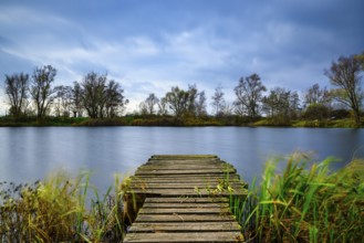 The beautiful blue lake with trees and the cloudy sky in background and a wooden path leading to it