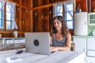 Smiling freelancer woman working on vacation inside a wooden mountain chalet, using a laptop
