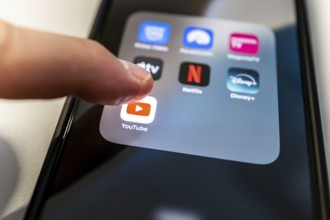 One finger touches the YouTube icon on a smartphone screen with various other streaming apps