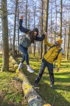 Hikers holding hands and balancing on a fallen tree trunk while enjoying a sunny day in a forest